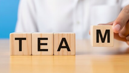Naklejka premium A hand placing the letter 'M' block to complete the word 'TEAM' spelled out with wooden blocks on a table, symbolizing teamwork and collaboration.