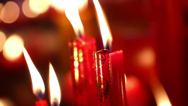 A group of candles in red are lit and arranged in a row. The candles are glowing brightly, creating a warm and inviting atmosphere. The candles are placed in a variety of positions