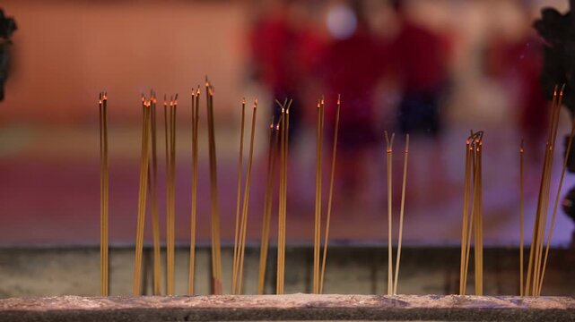A bunch of incense sticks are lit and are in a container. There are many incense sticks in the container