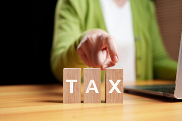 Tax concept with wooden blocks and hand pointing at TAX word on desk. financial responsibility, decision making, and personal or business taxation.