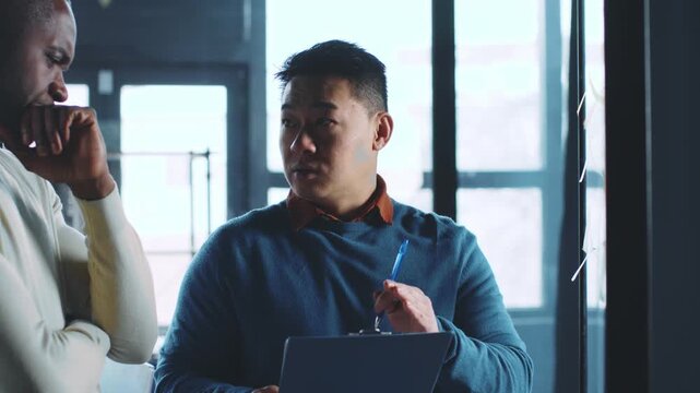 Two business professionals gather in a modern office to discuss important projects. One colleague listens thoughtfully while the other presents ideas using a tablet.