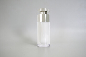A cosmetic bottle mockup for cream, serum, or lotion. The glass bottle features a pump dispenser and a metalized cap, isolated on a gray background