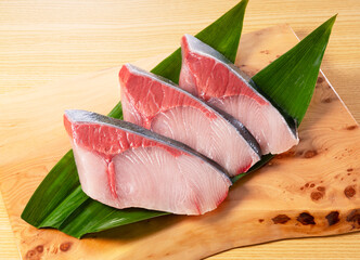 Fresh Japanese Yellowtail Fillets on Wooden Board with Bamboo Leaves.