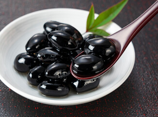 Japanese Traditional New Year Dish: Sweetened Black Soybeans (Kuromame) on a Spoon and Plate with Copy Space