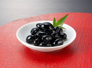 Traditional Japanese New Year Dish: Glossy Sweetened Black Soybeans (Kuromame) on a White Plate and Red Tray with Copy Space