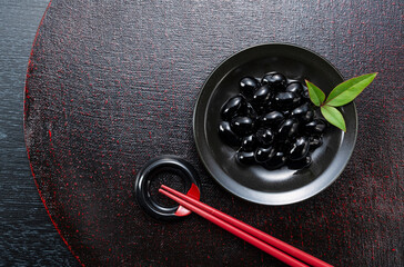Traditional Japanese New Year Feast: Glossy Sweetened Black Soybeans (Kuromame) on a Black Plate with Red Chopsticks and Copy Space