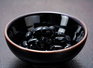 Glossy Sweetened Black Soybeans (Kuromame) on a Dark Ceramic Plate, Traditional Japanese New Year Dish with Copy Space