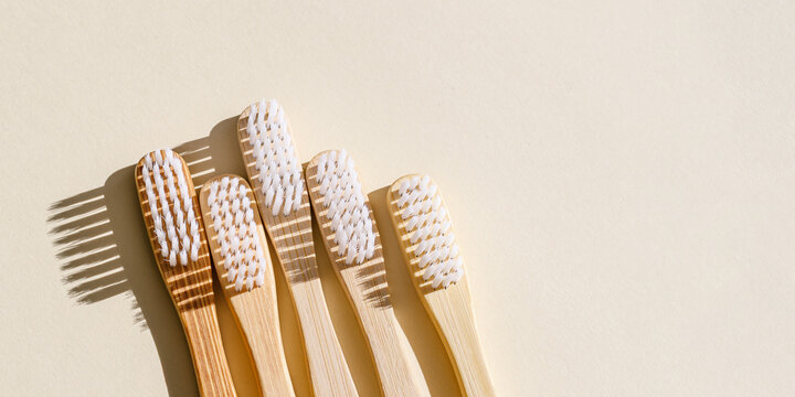 Aesthetic Beige bamboo toothbrushes with white bristles at sunlight on beige banner. Simplicity, hygiene, and environmentally friendly alternatives, top view photo, minimal flatlay neutral color