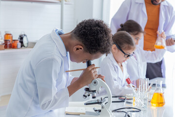 Close-up African boy and multicultural elementary students girl kids wearing lab coat uniforms using microscope with teacher in laboratory room, lifestyle pupil learning education in science class