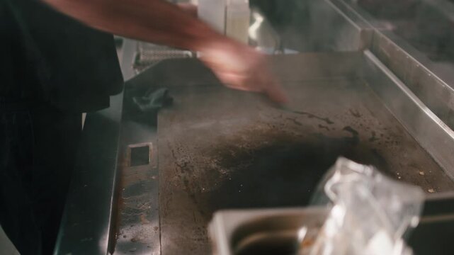 Professional chef cleaning a hot griddle in a restaurant kitchen