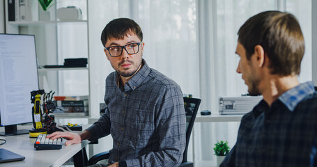 Adult male engineer team discusses AI software development robotic hand project use AI code solutions at tech workspace. Artificial intelligence interface, collaboration support prototype development.