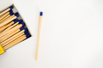 A wooden match with a blue head lies next to an open matchbox, isolated on a white background