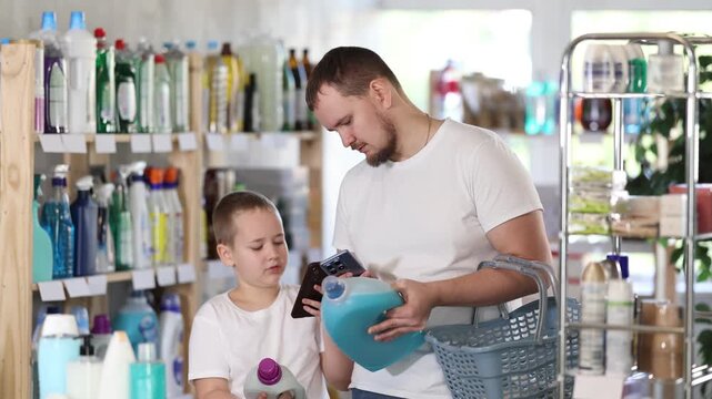 Dad and son scan barcode on packaging of laundry conditioner, looking for information about product on website. Boy watches actions of dad, learns to scan QR code using phone camera
