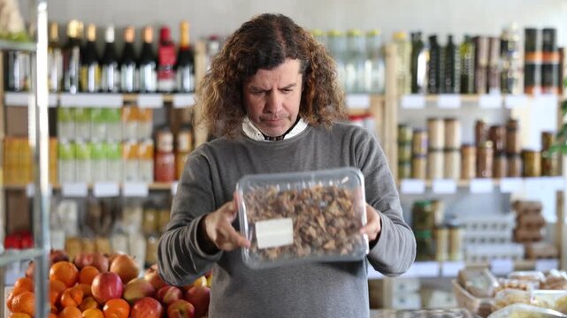In store, man near counter looking at murex brandaris. Visitors make choice of assortment, select buy chilled seafood. Customer read label, examine customer information, view package content