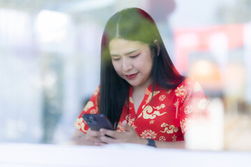 Portrait of asian woman wearing red cheongsam dress holding red envelopes and smartphone at home in the living room indoor decoration for Chinese new year festival celebrate culture of china holiday