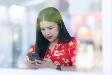 Portrait of asian woman wearing red cheongsam dress holding red envelopes and smartphone at home in the living room indoor decoration for Chinese new year festival celebrate culture of china holiday