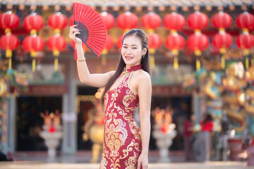 Portrait beautiful smiles Asian young woman wearing red traditional Chinese cheongsam decoration and holding a Chinese Fanning for Chinese New Year Festival at Chinese shrine in Thailand