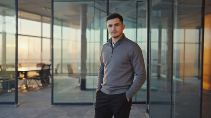 Young man in stylish casual clothes standing in front of shelves inside office.