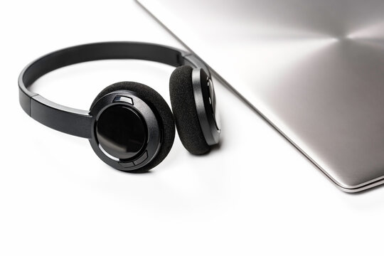 Stylish wireless headphones lying next to closed laptop on minimalist background. Modern work style.