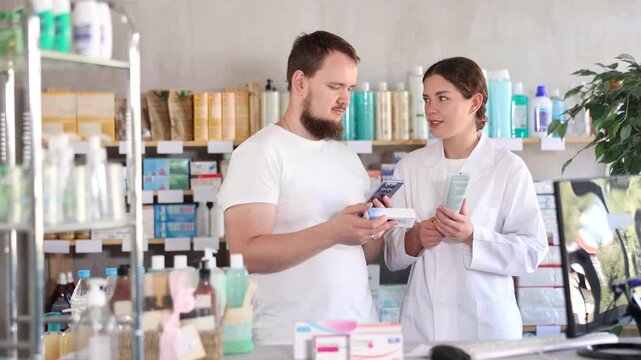 Young man buyer scanning qr code for box of ointment with young woman pharmacist in pharmacy
