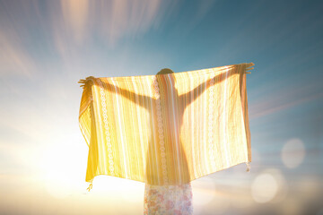 Backlit silhouette of a woman holding a flowing fabric against sunrise sky, symbolizing freedom, mindfulness, spiritual awakening, wellness lifestyle, inner peace, and positive energy in nature.
