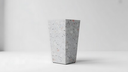 A tall geometric planter with a speckled terrazzo pattern featuring gray white and subtle pink flecks stands on a minimalist white surface with soft studio lighting creating a clean and modern