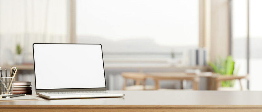 White screen laptop with books and pencils on wooden counter table across window wall in living room