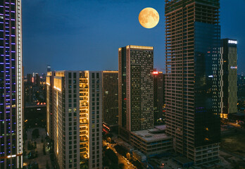 Obraz premium Full Moon Rising Over Illuminated City Skyscrapers at Night