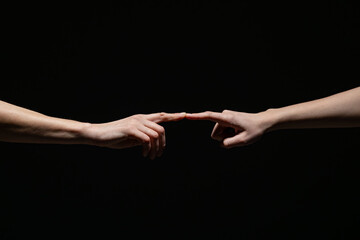 Two outstretched hands gently connect at the fingertips, evoking a sense of creation, unity, or intimacy against a deep black background with copy space