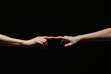 Two outstretched hands gently connect at the fingertips, evoking a sense of creation, unity, or intimacy against a deep black background with copy space