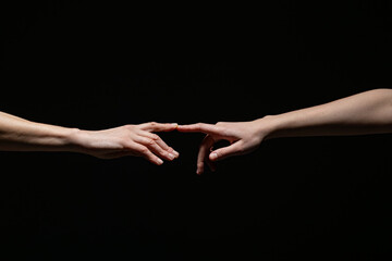 Two outstretched hands reach toward each other, fingers nearly touching, against a dark background. Symbolizes connection, longing, or creation with ample copy space