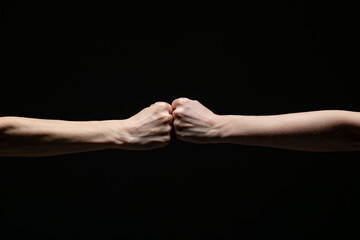 Two fists meet in a firm fist bump, symbolizing unity, strength, or solidarity, set against a dramatic black background. Minimalist composition with strong contrast