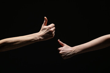 Two extended arms give thumbs-up gestures toward each other, symbolizing approval, positivity, or agreement, against a dark background with strong contrast