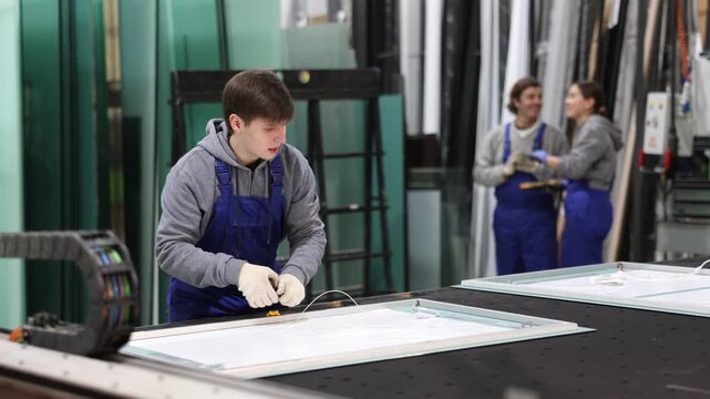 Guy employee works on cutting table, measuring source material with tape measure. She finds out length of workpiece and carries out intermediate control of dimensions of product.