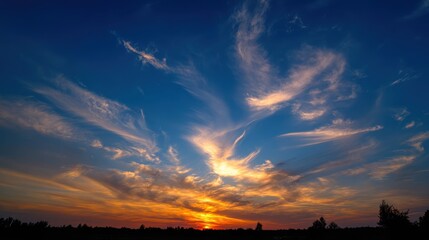 Dramatic sunset sky with wispy clouds over a silhouetted landscape