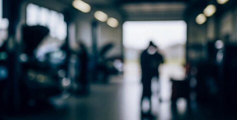 Blurry view inside vehicle repair shop with dark figure near exit, creating a moody industrial atmosphere with soft light contrast, shallow focus, and abstract visual depth.