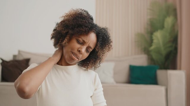 Black woman doing gymnastics for neck at home, prevention of osteochondrosis. Adult african american lady training and feeling pain in muscles, care about health and good feeling, yoga and stretching