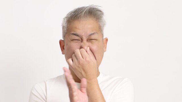 4K video of a middle-aged gray-haired man using hand holding nose feeling disgusted on white background