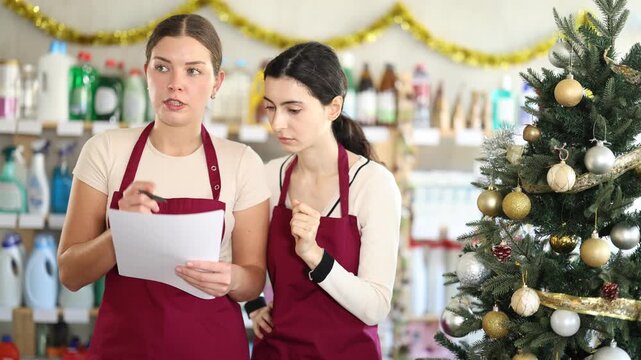 Two attentive saleswomen making notes on paper for restocking in store with New Year decoration . High quality 4k footage