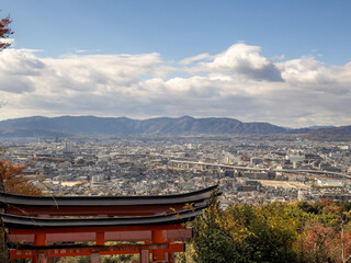 Panoramic view of Kyoto city from Fushimi Inari-taisha, featuring traditional orange torii gates and surrounding mountains on a cloudy autumn day.