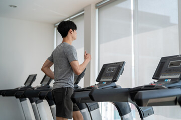 Asian young sportsman exercise by running on treadmill in gym club. 