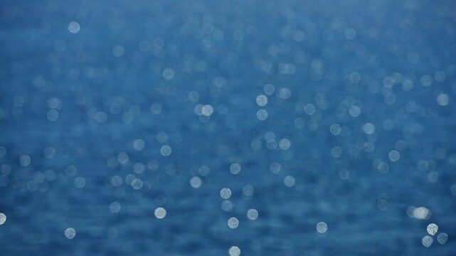 Blurry sea with glowing light. Soft bokeh sparkles on the ocean. Glowing water shimmers gently. Blurry waves catch the light. Ocean surface shines with bokeh. Sea glow creates calm mood.