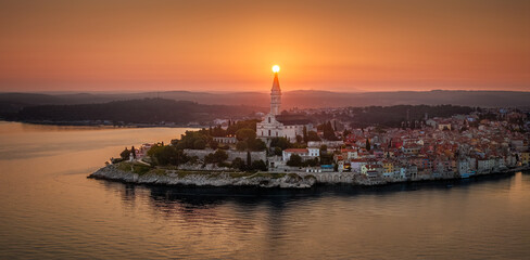 Rovinj, Croatia - Aerial panoramic view of the old town of Rovinj with Church of St. Euphemia and rising sun on a summer morning in Istria, Croatia. Golden sky and red rooftops by the Adriatic sea