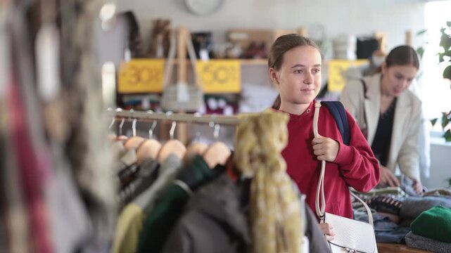 Positive teen girl customer looking for little shoulder bag during sell-out in retail outlet