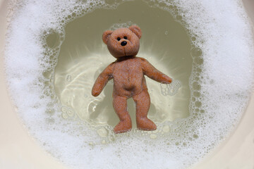 A teddy bear floating in soapy bubble water.
