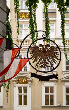 Schild mit einem stilisierten Doppeladler und rot-wei&szlig;en Fahnen an einer Hausfassade in der Wiener "Griechengasse"