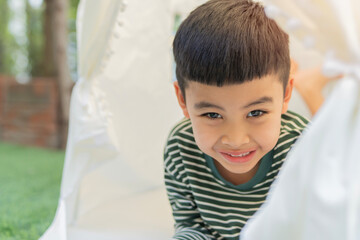 Portrait of happy 5 years old little Asian boy lying down in a wigwam tent in the garden at home © Kunlathida