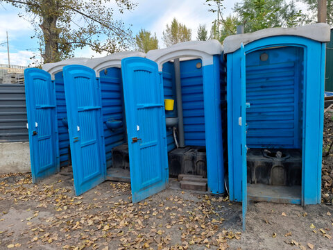 Blue plastic outdoor toilet cabins with open doors near construction site