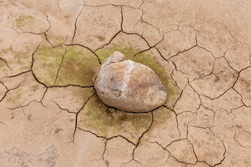Dry cracked earth and weathered stones create an abstract brown texture across an arid desert land of parched clay and sand