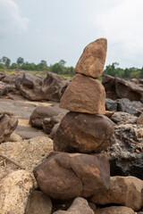 A scenic travel landscape features blue sky and white clouds over granite rocks and stones on a beach by the ocean and mountain cliffs